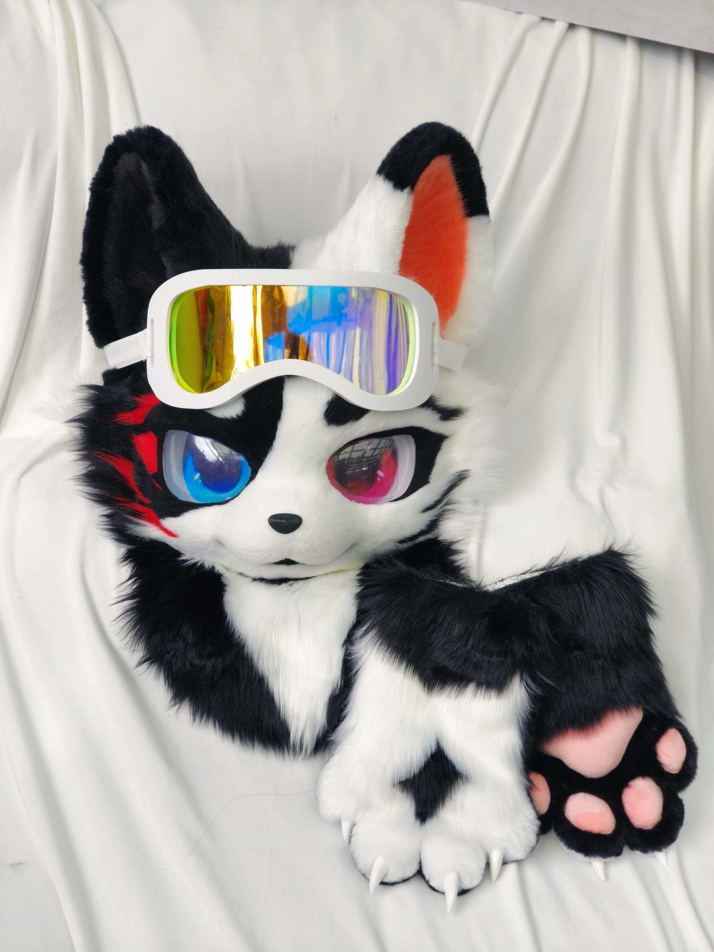 Black and white kemono wolf fursuit partial with heterochromia eyes, red streak, rainbow goggles and paw props